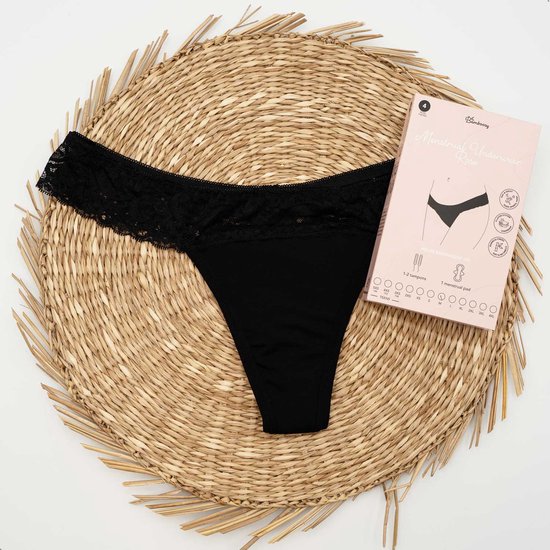 String noir en dentelle sur un dessous de plat en osier, à côté d'un emballage rose de sous-vêtements menstruels Bamboozy 'Roos'.