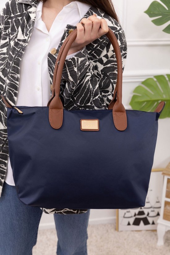 Gros plan sur un sac en nylon bleu foncé avec anses en cuir marron et un logo doré.