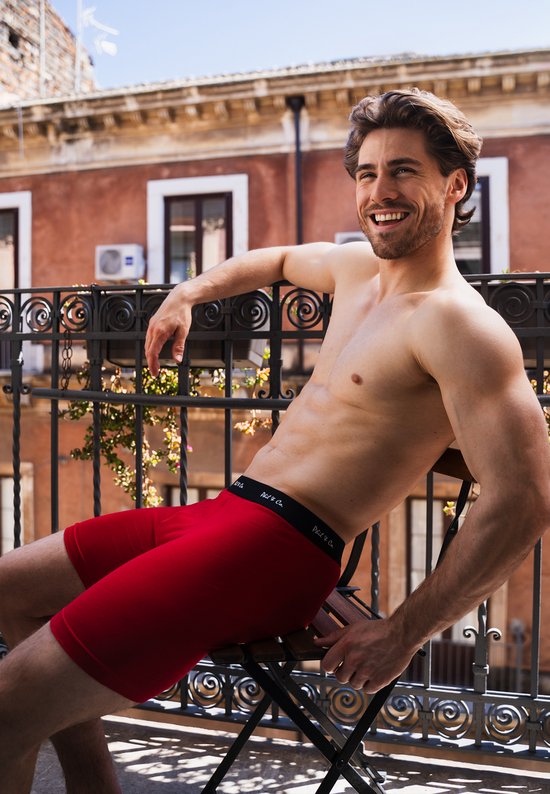 Homme en caleçon rouge, assis sur un balcon, avec logo sur la ceinture.