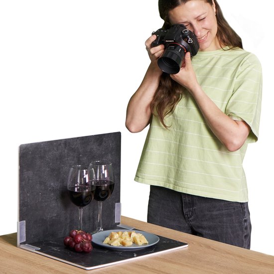 Vrouw fotografeert met digitale camera, statief met twee wijnglazen en druiven met kaas. Witte achtergrond.