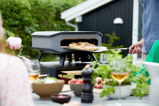 Hand met pizzalepel haalt pizza uit een Cozze pizzamaker.