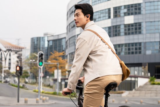 Un homme fait du vélo en ville, portant un écouteur Shokz noir.