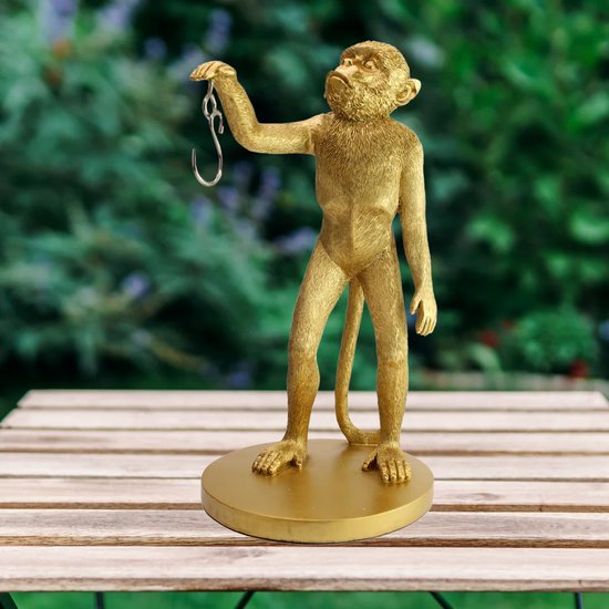 Gouden aap figuur op een houten tafel, met een lege haak in de hand.