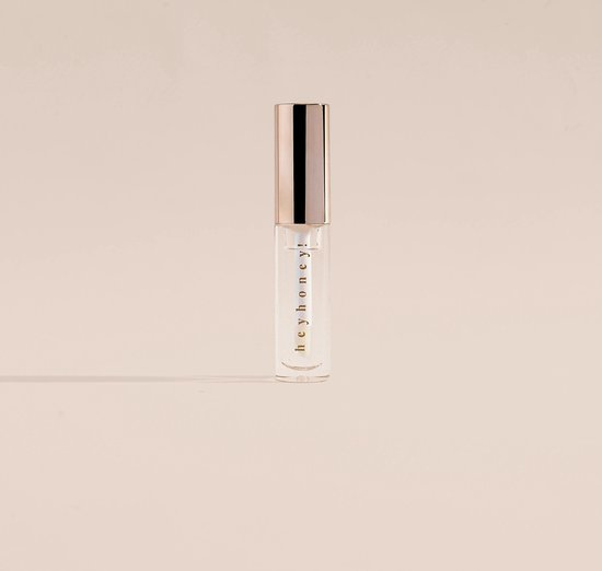 Transparante lipgloss tube met "hey honey!" erop en een gouden dop, op een egale achtergrond.