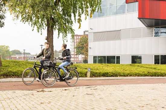 Twee jongens fietsen op stadsfietsen met kratten voorop, langs een gebouw.