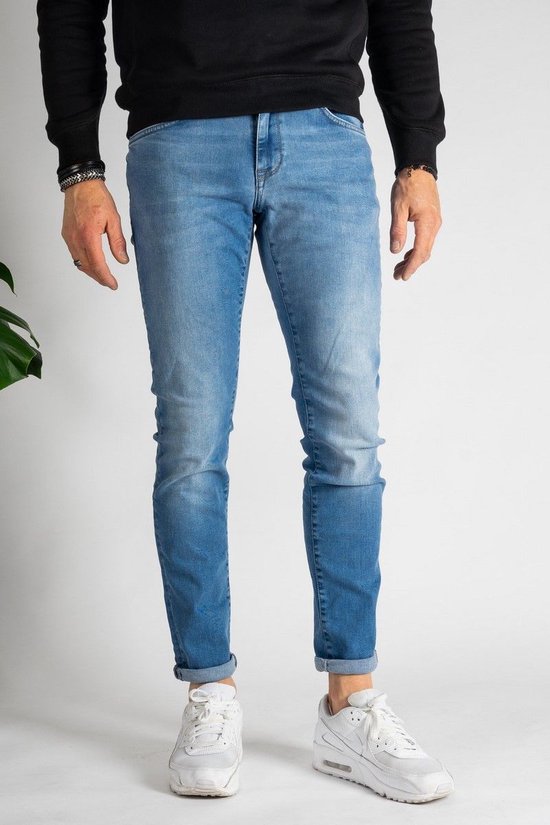 Man in een lichtblauwe spijkerbroek met een opgerolde zoom, witte sneakers en een zwarte trui.