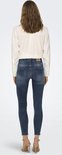 Achterkant van een model in een blauwe skinny jeans met rafels aan de zoom.