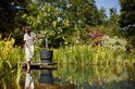 Een vrouw in een wit pak staat naast een vijgenboom in een grote zwarte bloempot.
