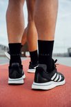 Pieds de coureurs portant des chaussettes Falke noires et des chaussures Adidas noires, courant sur une piste d'athlétisme.