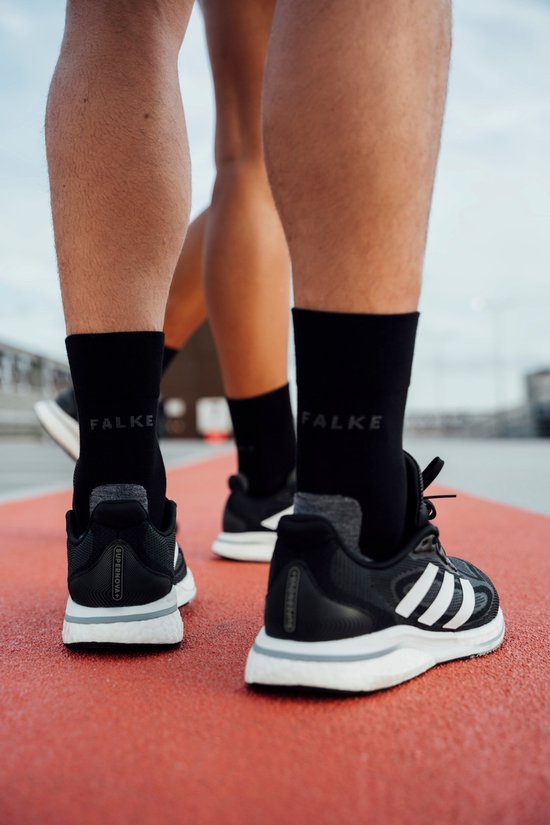 Pieds de coureurs portant des chaussettes Falke noires et des chaussures Adidas noires, courant sur une piste d'athlétisme.