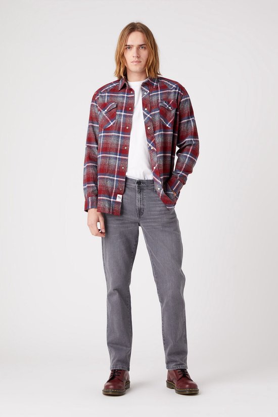 Man met lang blond haar draagt een grijs straight-fit jeans en een rood geruit flanellen overhemd.