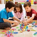 Drie kinderen spelen met veelkleurige magnetische bouwtegels op de vloer.