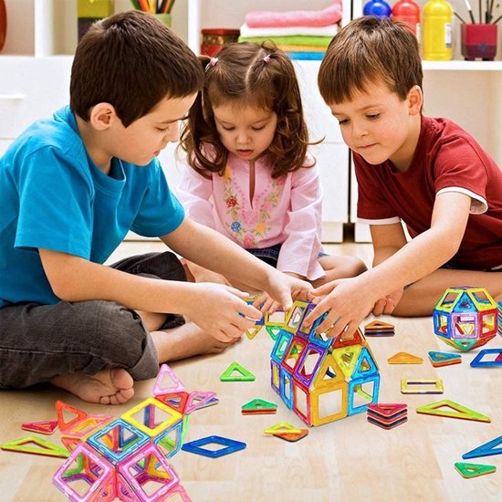Drie kinderen spelen met veelkleurige magnetische bouwtegels op de vloer.