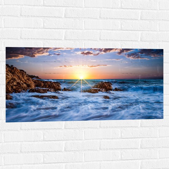 WallClassics - Muursticker - Felkleurige Zonsondergang achter Wilde Zee - 100x50 cm Foto op Muursticker