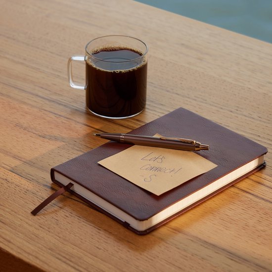 Carnet bordeaux fermé avec un stylo posé dessus. Une note disant 'Let's Connect!' est sur le carnet. Une tasse de café est à côté.