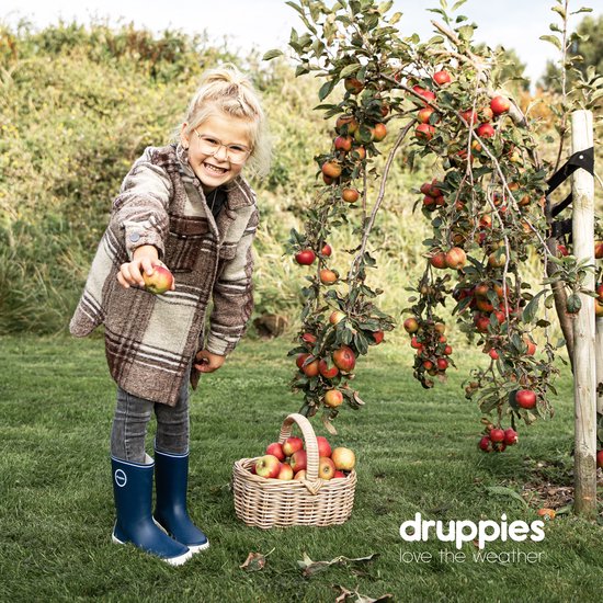 Lachend meisje met blonde paardenstaart, draagt een geruite jas, grijze jeans en donkerblauwe rubberlaarzen, in een boomgaard met appels.