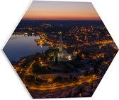 PVC Schuimplaat Hexagon - Kerkje in Midden van Verlicht Stadje - 40x34.8 cm Foto op Hexagon (Met Ophangsysteem)