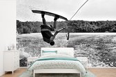 Behang - Fotobehang Een mannelijke tiener hangt ondersteboven op een wakeboard - zwart wit - Breedte 600 cm x hoogte 400 cm