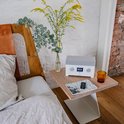 Witte Teufel radio met grijs rooster op een nachtkastje naast een bed, met bloemen en een glas.