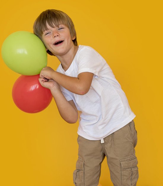 Jongetje met grote ogen houdt groene en rode ballonnen vast.