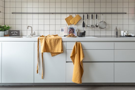 Gele keuken met een witte tegelwand, aan de muur hangen gele ovenwanten.