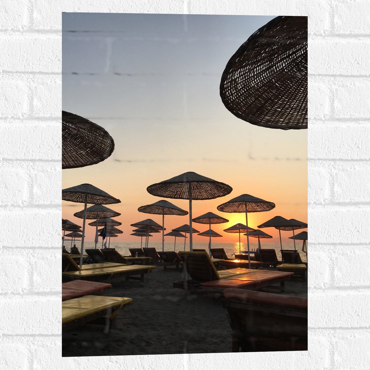 Muursticker - Ligbedden met Rieten Parasols aan het Strand in de Avondzon - 40x60 cm Foto