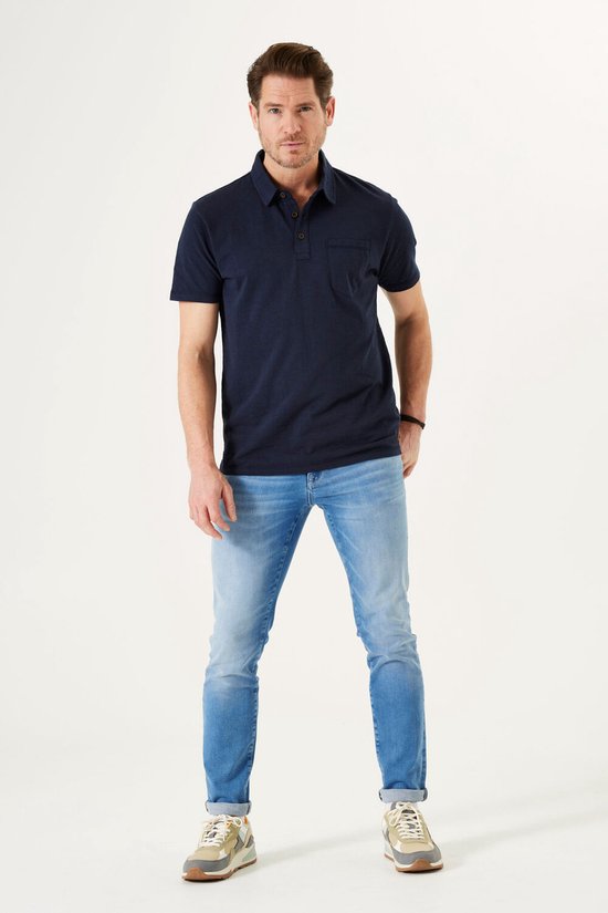 Man met donkerblauwe polo en lichtblauwe jeans, staand naar voren.