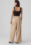 Model van achteren gezien draagt zwarte top met kanten details op de schouderbandjes en beige wijde broek.