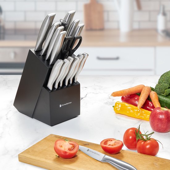 Een KitchenBrothers messenset in een zwart blok, met groenten op de achtergrond en een tomaat op een snijplank.