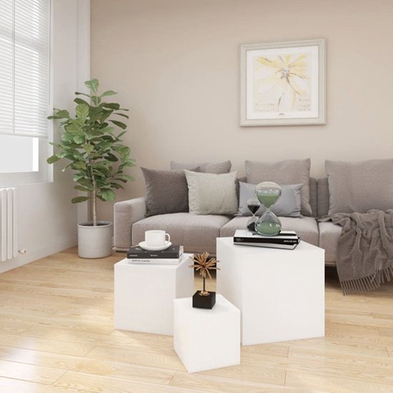 Woonkamer met witte kubus bijzettafels, waar een plant, kussen, zandloper en boeken op staan.