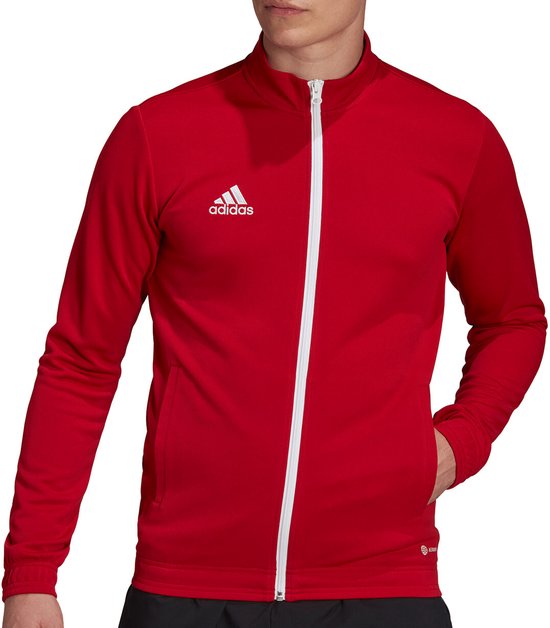 Man met lange rode jas, witte ritssluiting en adidas logo op de borst. Hand in zak.