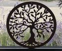 Décoration murale ronde en bois marron avec un motif d'arbre de vie, devant des fleurs violettes.