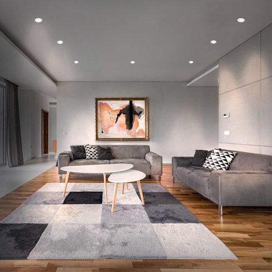Moderne woonkamer met grijze banken, witte salontafels en grijze vloerlampen.