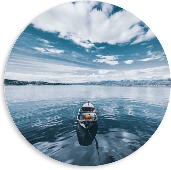 Un bateau flotte sur l'eau sous un ciel bleu et nuageux avec des montagnes à l'arrière-plan.