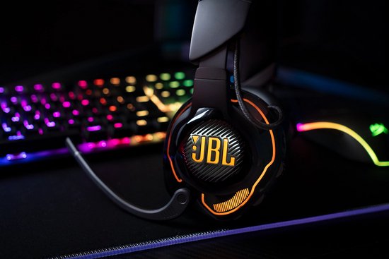 Zwarte JBL Quantum gaming headset met oranje accenten, naast een verlicht toetsenbord en muis.
