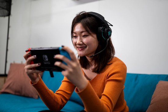 Vrolijke Aziatische vrouw met een zwarte JBL Quantum headset, spelend op een Nintendo Switch.