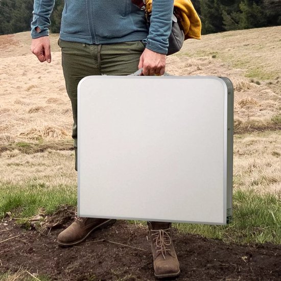 Persoon met opgevouwen lichtgrijze tafel in een grasrijke omgeving.