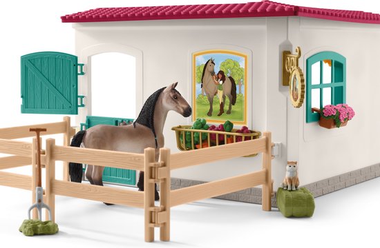 Een speelgoedpaard staat in een stal met een houten hek en een mand met groenten.