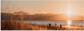 WallClassics - Poster Glanzend – Zon Verdwijnend achter Bergen bij Strand - 60x20 cm Foto op Posterpapier met Glanzende Afwerking