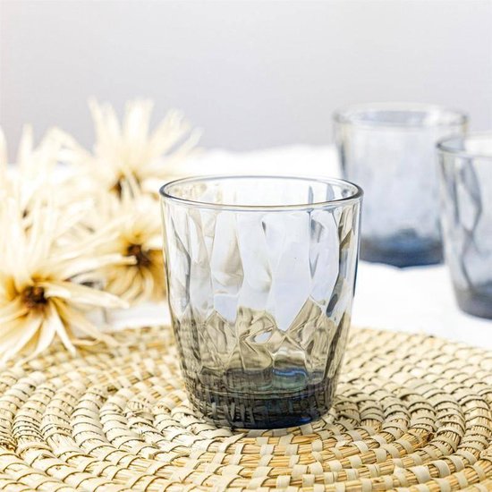 Un verre à eau Bormioli Rocco Diamond au motif facetté, posé sur un dessous de plat en osier.