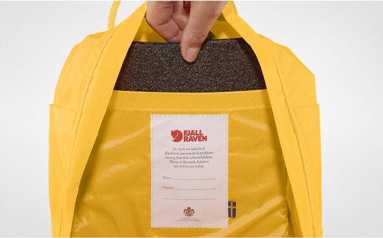 Gele Kånken rugzak met een label en een hand die een zwart kussen erin stopt.