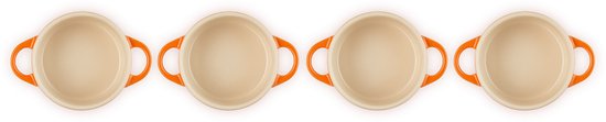 Vier lege, crèmekleurige mini-braadpannen met oranje handvatten, van bovenaf gezien.