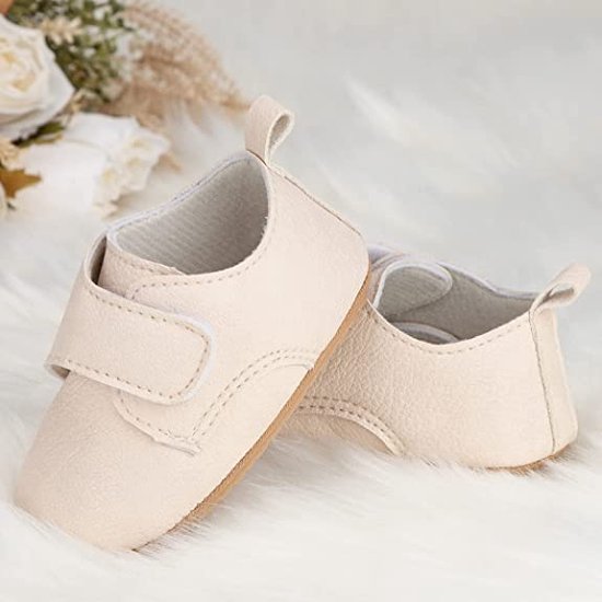 Beige babyslofjes met klittenbandsluiting, op een zachte witte achtergrond met bloemen.
