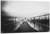WallClassics - Tuinposter – Persoon op Brug bij het Water in het zwart-wit - 120x80 cm Foto op Tuinposter  (wanddecoratie voor buiten en binnen)