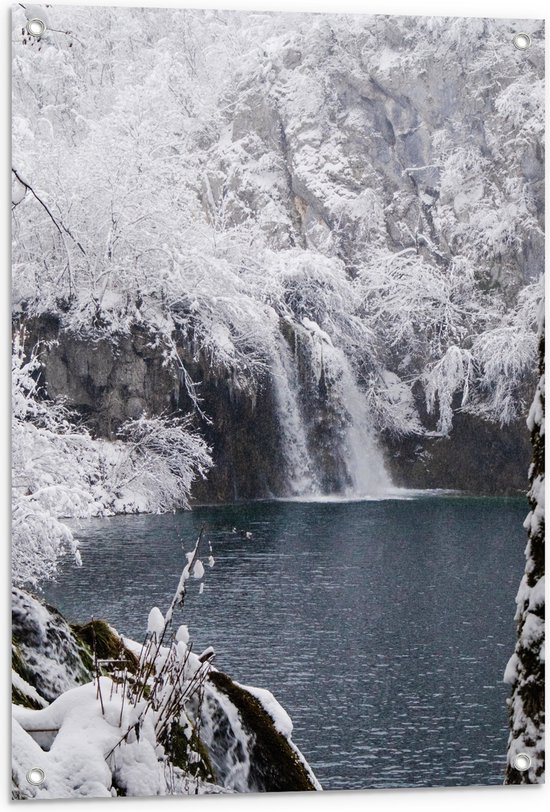 Besneeuwde bomen en rotsen rondom een waterval en een blauw meer.