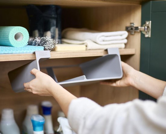 Mains plaçant un organisateur Joseph Joseph gris sous une étagère dans une armoire de cuisine.