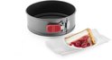 Grijze ronde springvorm met rode sluiting, naast een punt cheesecake met kersen.