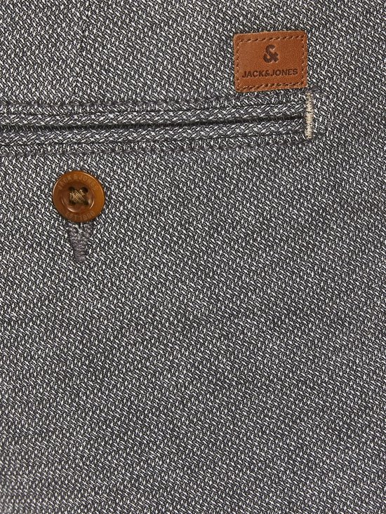 Grijze broek met visgraatpatroon en een bruine knoop, met een bruin label van Jack & Jones op de achterzak.