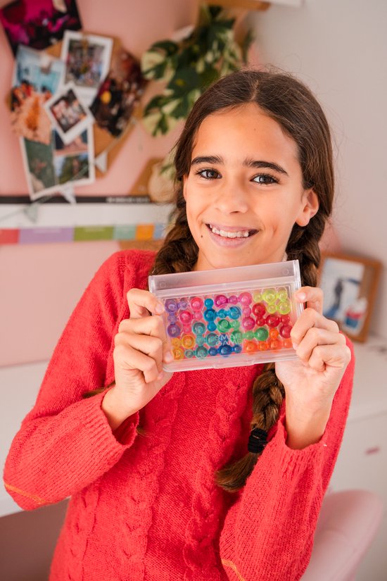 Lachend meisje met vlechtjes houdt een gevuld speldoosje met kleurrijke bubbels vast.