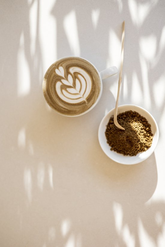 Witte mok met latte art, naast een schaaltje met hojicha poeder en een bamboe schepje, op een lichte ondergrond met schaduwen.